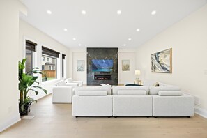 Ein modernes Wohnzimmer mit Kamin, weißen Sofas, einem großen Gemälde und Blick durch das Fenster.