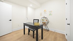Una habitació amb taula negra, una cadira, una làmpada d'escriptori i una petita estanteria hexagonal amb llibres i una planta.