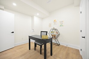 Ein Zimmer mit einem schwarzen Tisch, einem Stuhl, einer Schreibtischlampe und einem sechseckigen Regal mit Büchern und einer kleinen Pflanze.