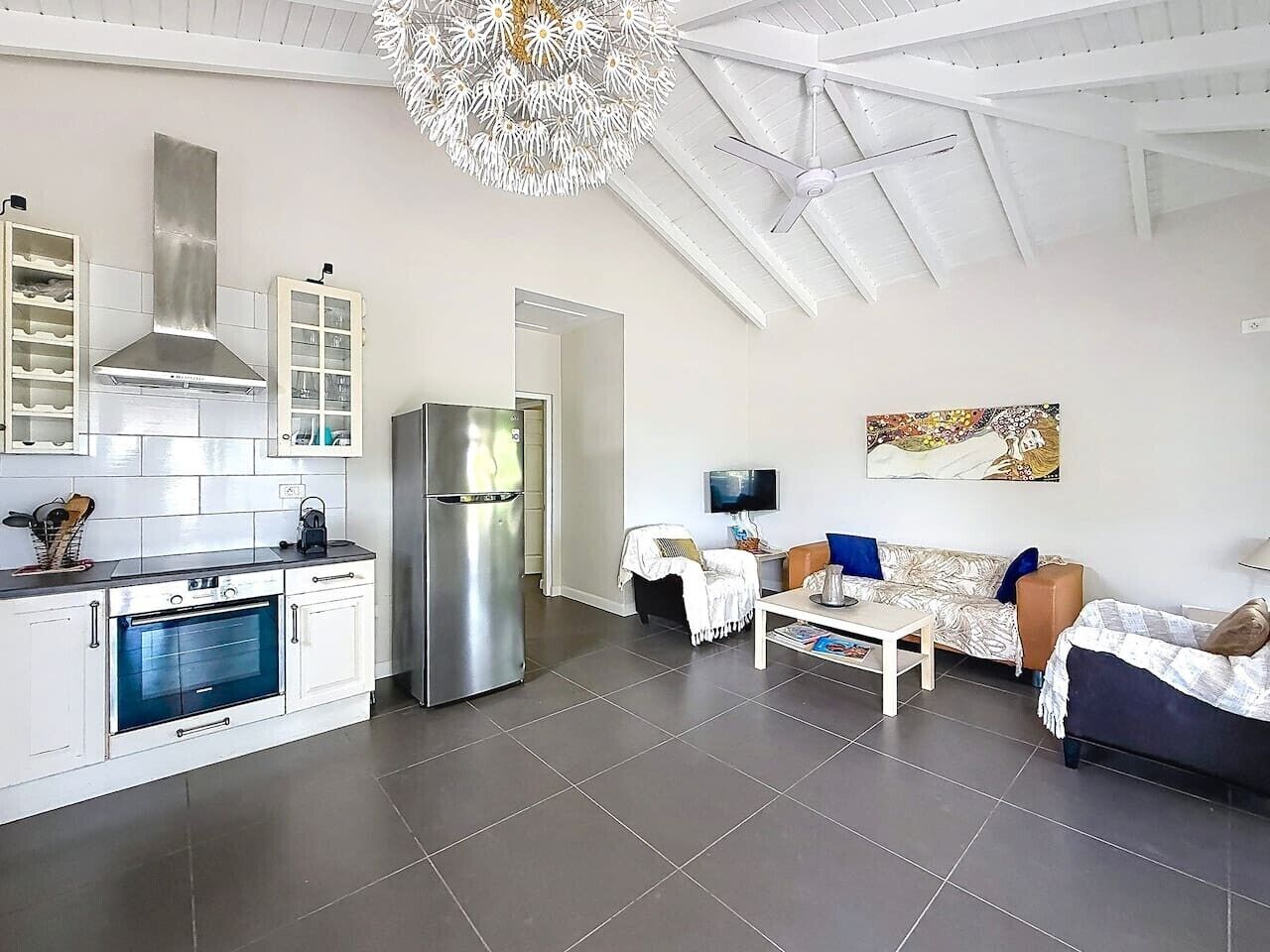 Eine moderne Küche mit Einbaugeräten, ein Essbereich mit Sofa und Tisch sowie ein Wohnzimmer mit Fernseher.