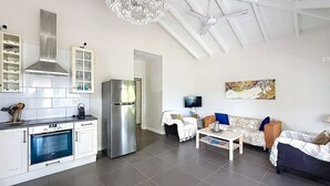 A modern kitchen with built-in appliances, a dining area with a sofa and table, and a living room with a television. - Villa Sunrise Blue – Peaceful Retreat with Bay Views in Cul-de-Sac (Cul-de-Sac)