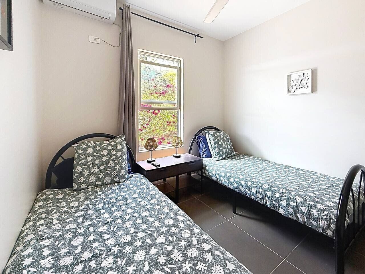 Ein Zimmer mit zwei Einzelbetten, einem kleinen Tisch und einem Fenster mit Vorhängen.