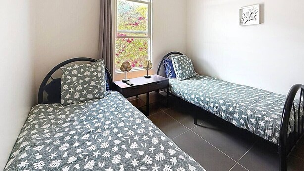A room with two single beds, a small table, and a window with curtains. - Villa Sunrise Blue – Peaceful Retreat with Bay Views in Cul-de-Sac (Cul-de-Sac)