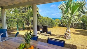 A covered outdoor dining area with a table set for two, surrounded by chairs, and a view of the ocean and tropical vegetation. - Villa Sunrise Blue – Peaceful Retreat with Bay Views in Cul-de-Sac (Cul-de-Sac)