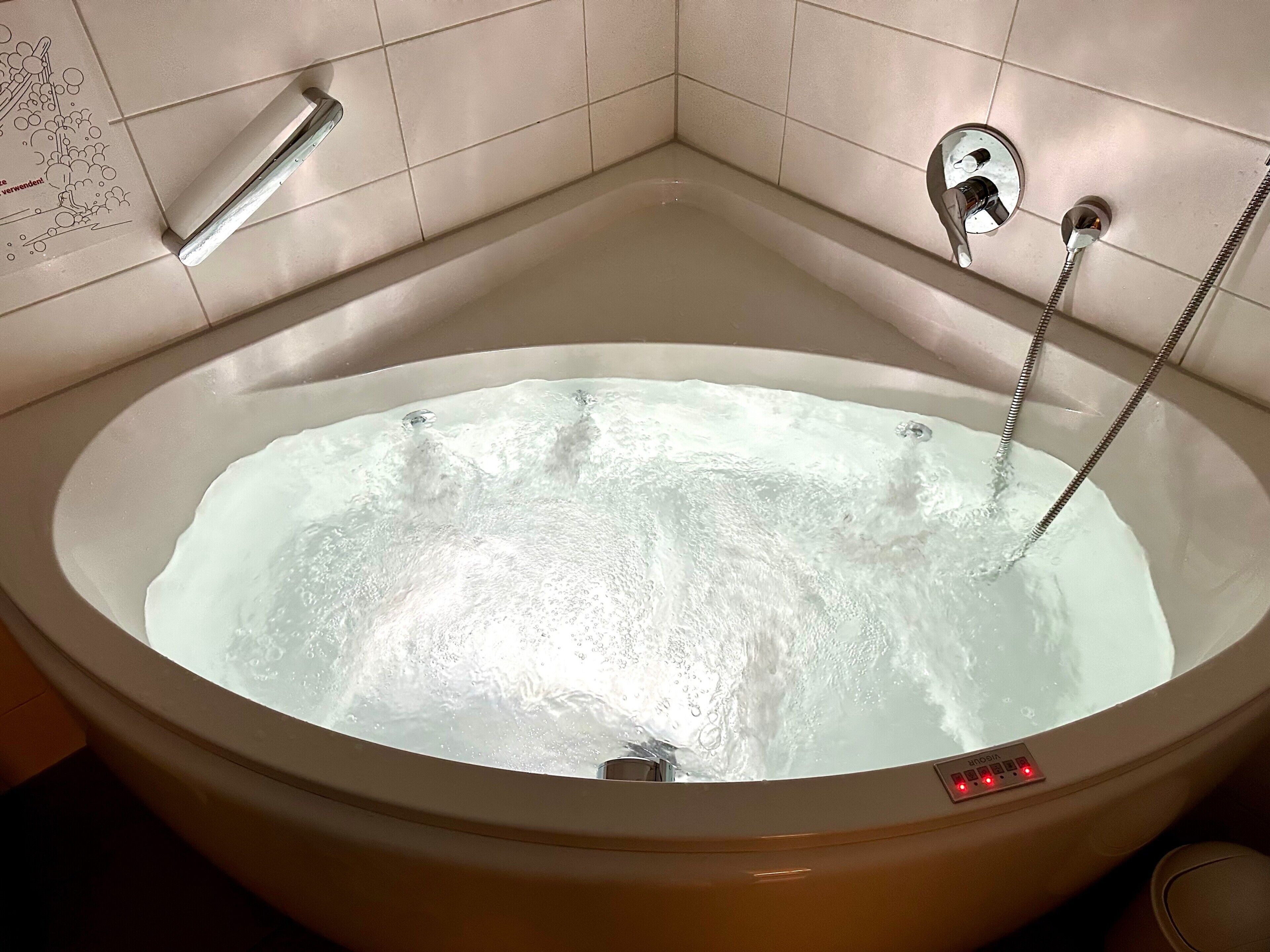 A bathtub with a control panel and a handheld showerhead.