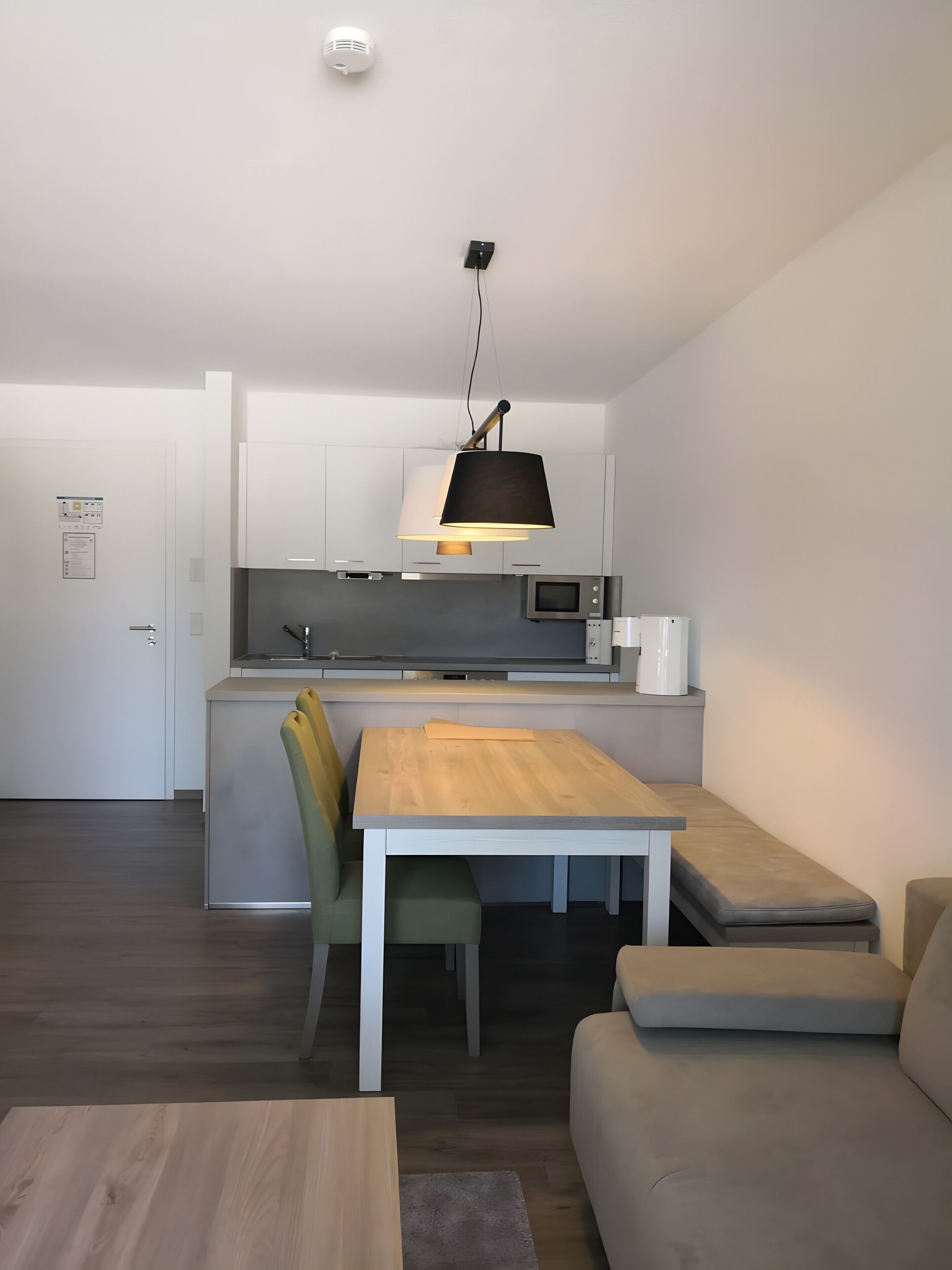 A modern kitchen with white cabinets, a wooden dining table, and a black pendant light.