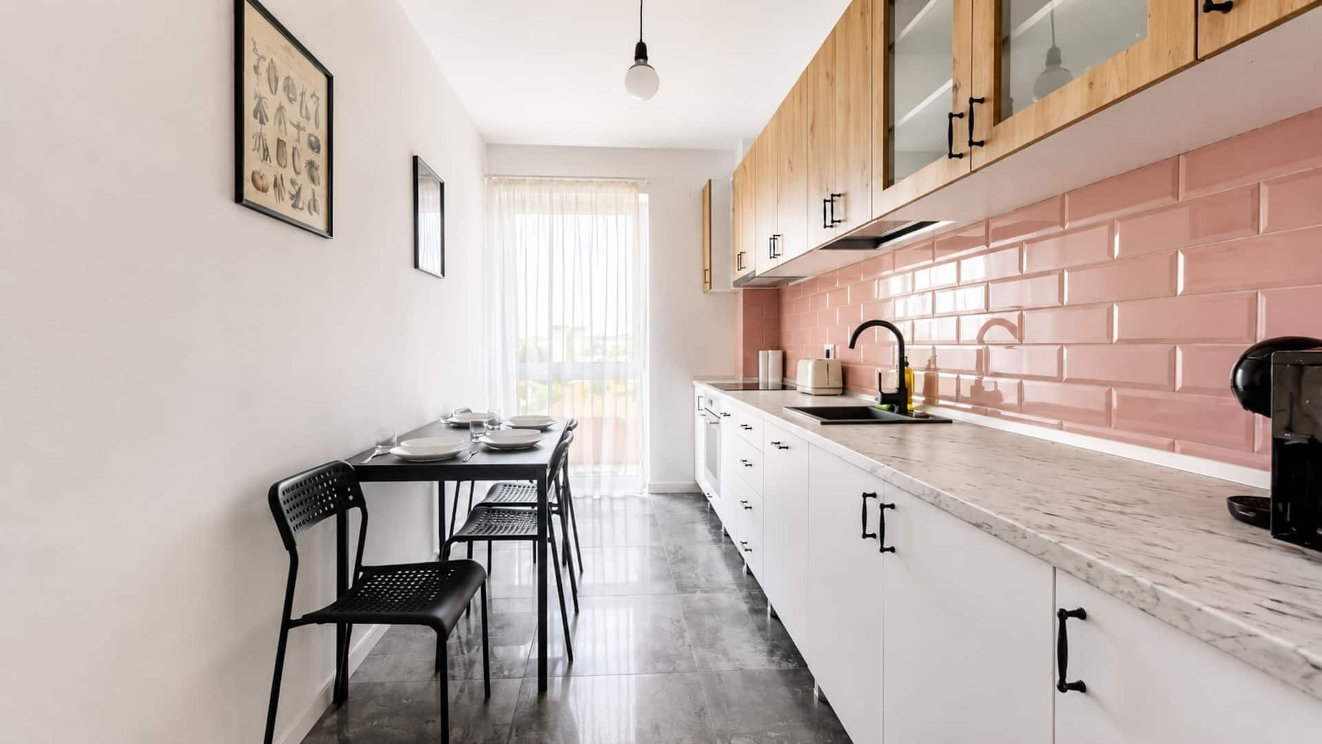 A modern kitchen with white cabinets, a pink backsplash, and a dining area with a table and chairs.