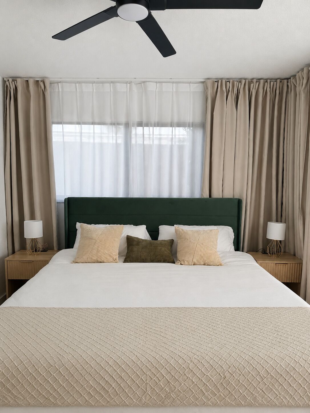 Una habitación de hotel con cama, ventilador de techo, cortinas y lámparas de noche.