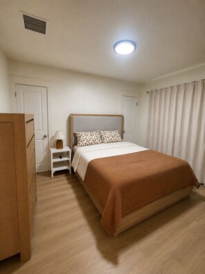 Een slaapkamer met een bed, nachtkastje, kaptafel en een plafondlamp.