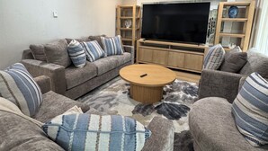 Una sala de estar con un conjunto de sofá, una mesa de centro, un televisor y una estantería.