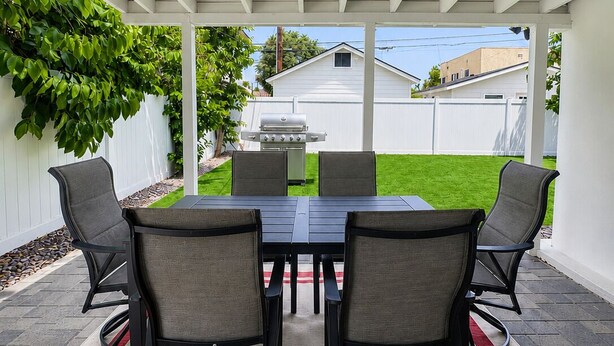 Un patio cubierto con mesa y sillas, una parrilla y vistas a una casa y jardín.