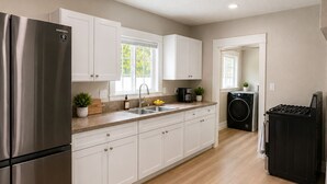 Una cocina moderna con armarios blancos, un refrigerador de acero inoxidable, un fregadero y un horno empotrado.