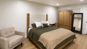 Un dormitorio con cama, una silla, armario y espejo.