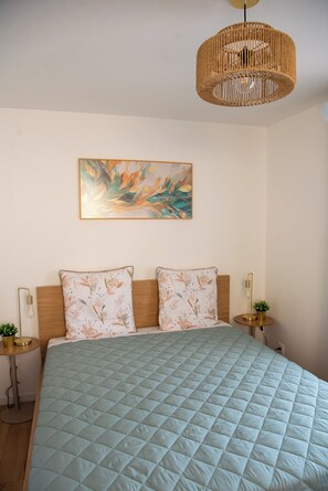 Un dormitorio con cama, lámpara colgante, cuadro en la pared y mesitas de noche con lámparas.