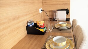 Un comedor ordenado con una mesa dispuesta para dos personas, incluyendo platos, vasos, cubiertos y una caja de aperitivos.
