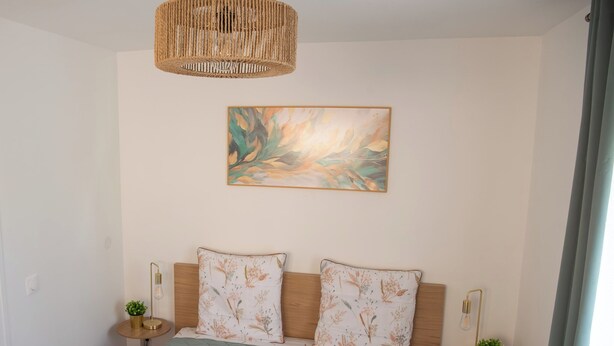 Un dormitorio con cama, dos mesitas de noche, una lámpara colgante y un cuadro en la pared.