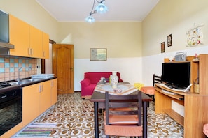 A compact living space with a kitchenette, a dining area with a table and chairs, a sofa, a television, and a decorative clock. - Apartment with Wi-Fi and Air Conditioning (Avola)