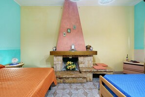 A bedroom with a stone fireplace, two beds, a nightstand, and a small table with a lamp. - Apartment with Wi-Fi and Air Conditioning (Avola)