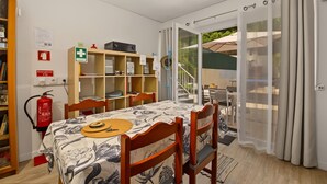 Ein Zimmer mit Esstisch, Stühlen, einem Bücherregal, einem Feuerlöscher und einer Glastür, die zu einem Außenbereich führt.