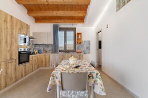 A compact kitchen with wooden cabinets, a microwave, and a table set for dining. - Attic with Sea View, Wi-Fi and Air Conditioning (Avola)