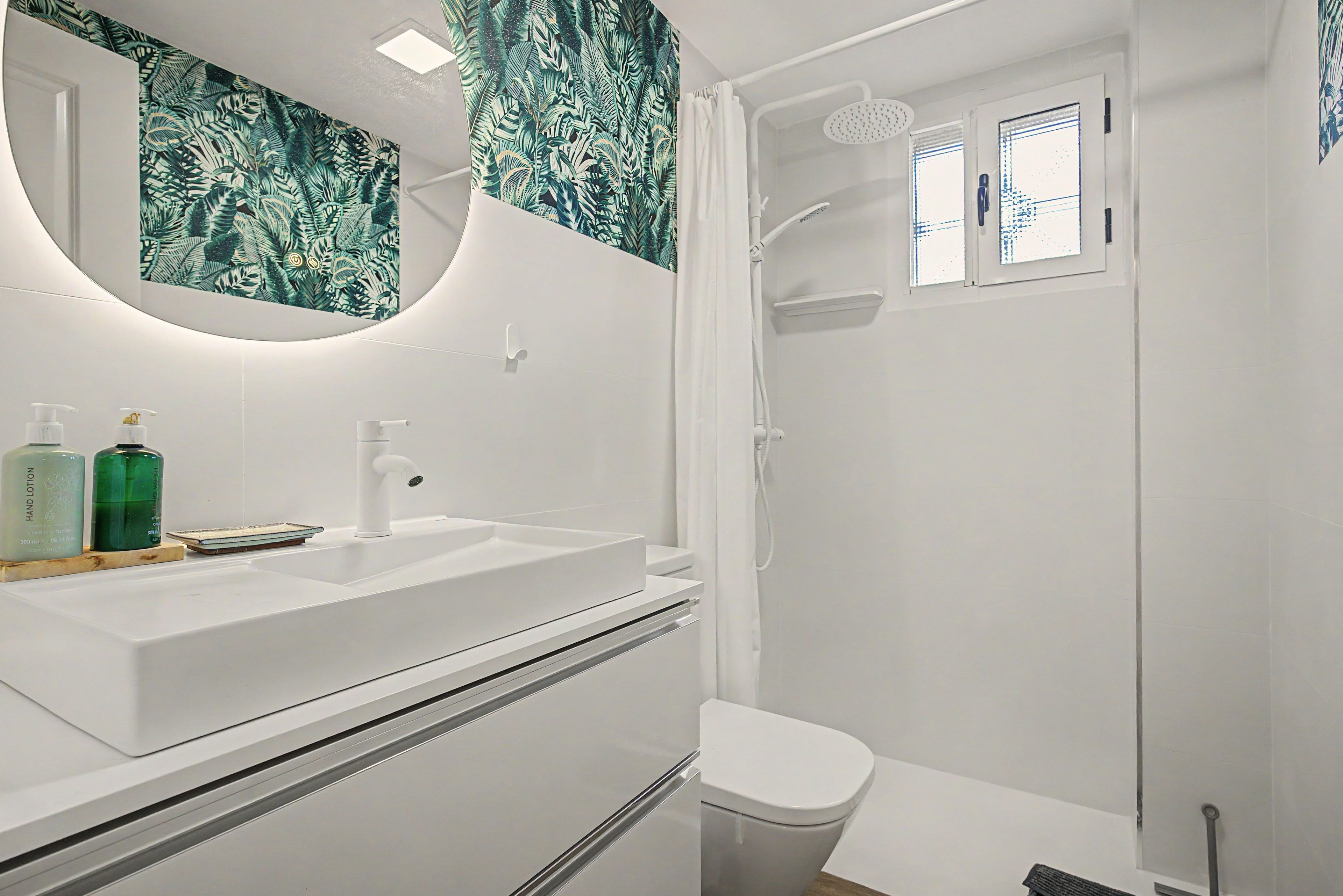 Een badkamer met een wit wastafelmeubel, een spiegel, een douche en een toilet.