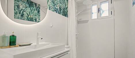 Een badkamer met een wit wastafelmeubel, een spiegel, een douche en een toilet.
