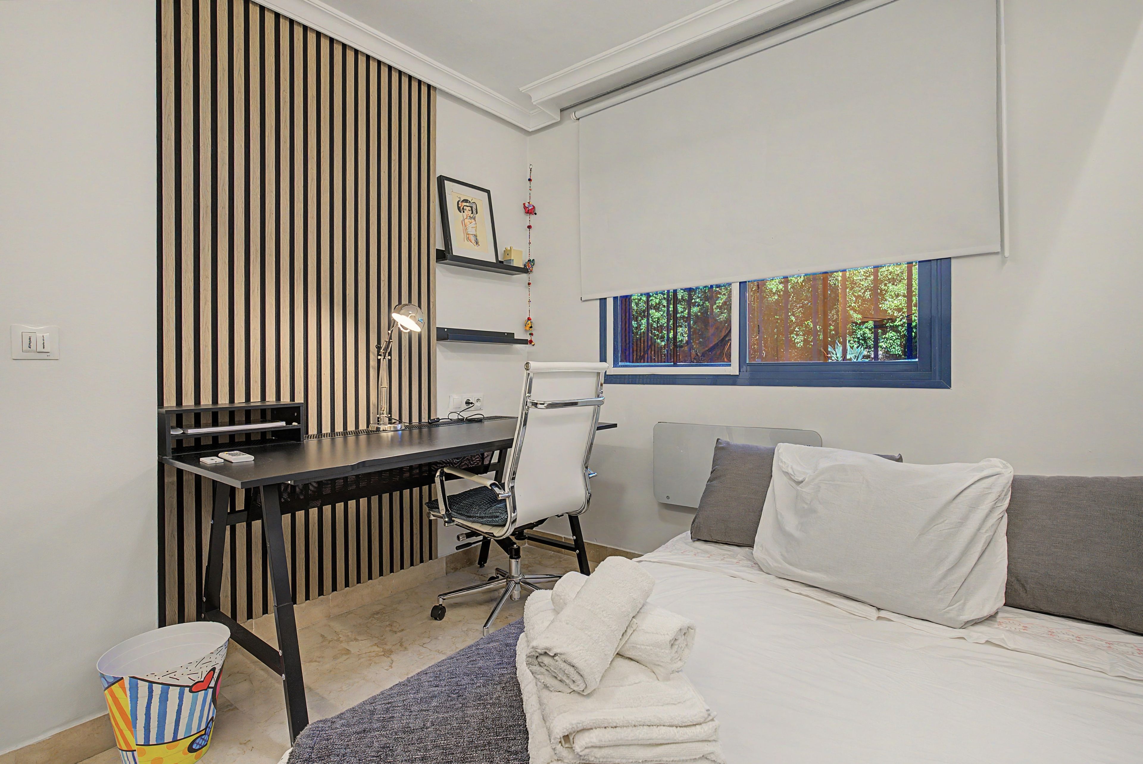 Un dormitorio moderno con un escritorio, una silla, una cama y una ventana con vistas a árboles.