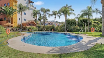 Una piscina con un bordeado, palmeras y un edificio con balcones.