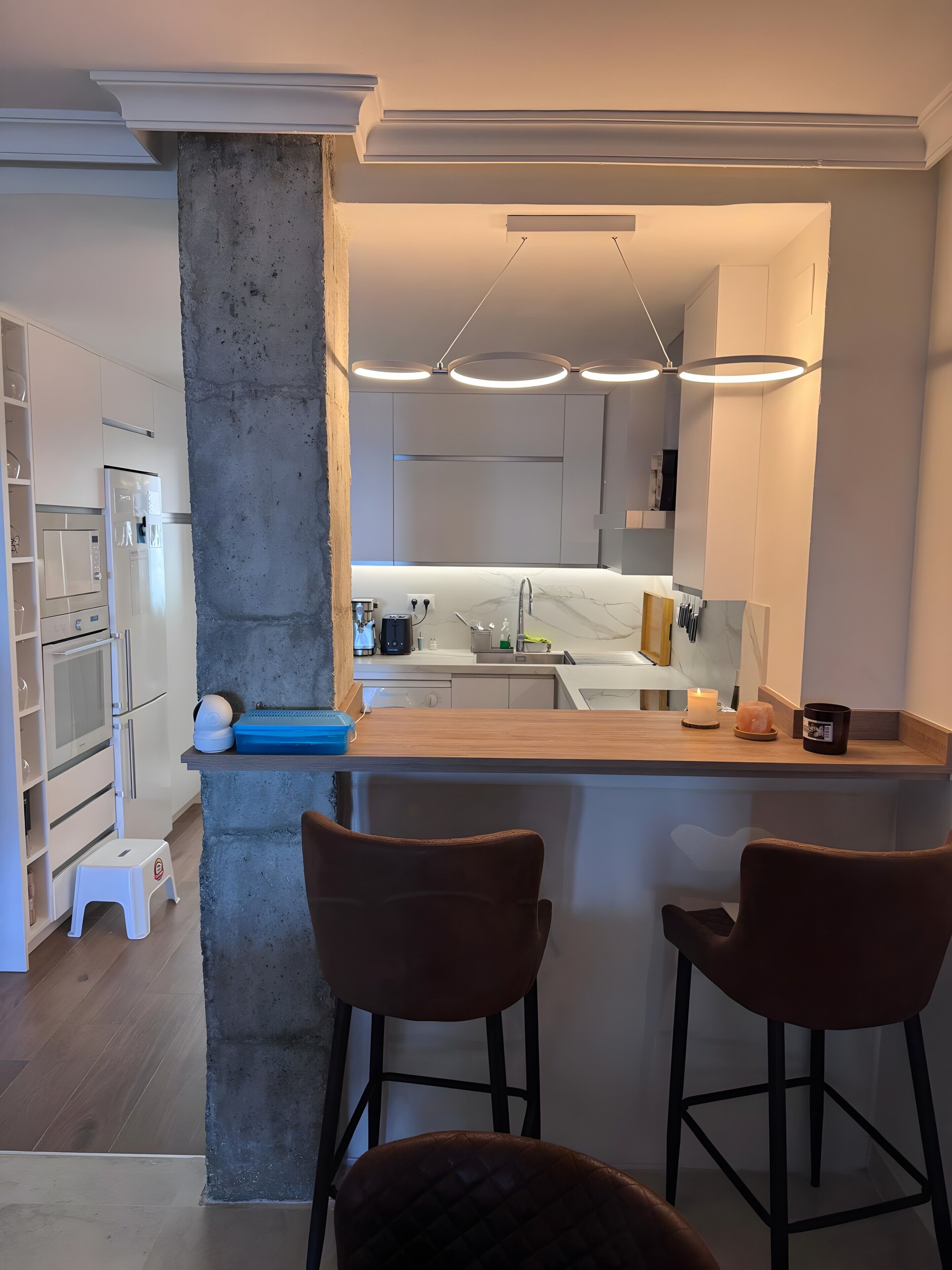 A modern kitchen with a central island, bar stools, and a large mirror.