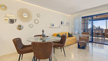 Una sala de estar moderna con una mesa de comedor de vidrio, sillas tapizadas en marrón, un sofá amarillo y espejos decorativos en la pared.