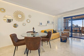 Una sala de estar moderna con una mesa de comedor de vidrio, sillas tapizadas en marrón, un sofá amarillo y espejos decorativos en la pared.