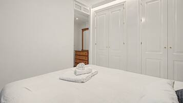 Een slaapkamer met een bed, een houten dressoir en een tweedeurs garderobe.