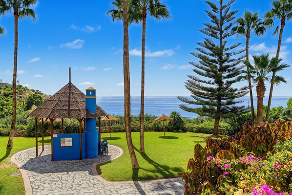 A tropical garden with a gazebo, palm trees, and a view of the ocean.