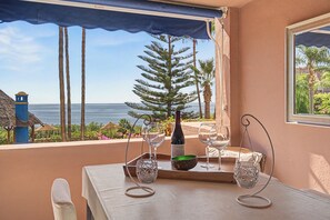 A table set with a bottle of wine, glasses, and a decorative bowl on a balcony overlooking the sea.