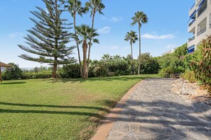 A landscaped garden with a stone pathway, palm trees, and a building with balconies. - Apartment 'Casa Soledad' with Sea View, Shared Pool and Wi-Fi (Almuñécar)