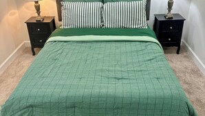 Makuuhuoneessa on sänky, kaksi yöpöytää, kaksi lamppua, sängynpääty ja vihreä päiväpeite.