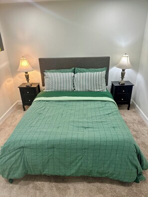 Ein Schlafzimmer mit einem Bett, zwei Nachttischen, zwei Lampen, einem Kopfteil und einer grünen Bettdecke.