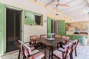 A dining area with a wooden table and chairs, green shutters, and a ceiling fan. - Villetta Fico d`India by BarbarHouse (Sant'Isidoro)