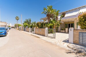 A residential street with houses, palm trees, and a blue car parked on the side. - Villetta Fico d`India by BarbarHouse (Sant'Isidoro)