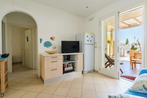 Um espaço compacto para viver com televisão em um suporte, um pequeno frigorífico, uma estante e uma porta de vidro deslizante que dá para uma área externa com um pátio.
