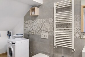 Ein modernes Badezimmer mit Waschmaschine, Handtuchhalter und gemusterten Fliesen.