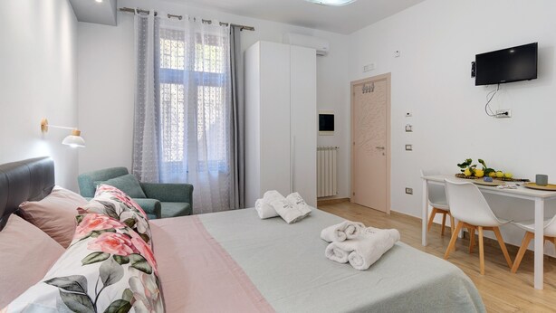 Ett modernt hotellrum med en säng, ett skrivbord, en stol, en TV och ett fönster med gardiner.