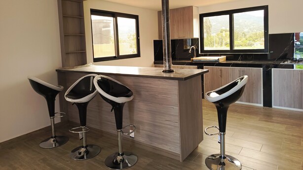 Una cocina moderna con una isla de madera, dos taburetes altos y ventanas amplias con vistas.