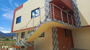 Un edificio de varios pisos con balcón, una escalera y vistas del paisaje circundante.