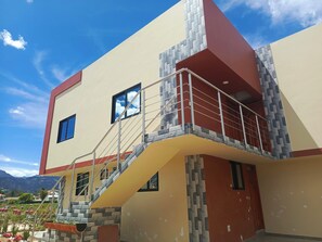 Un edificio de varios pisos con balcón, una escalera y vistas del paisaje circundante.