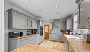 A modern kitchen with grey cabinets, a wooden countertop, and built-in appliances. - Greenways House - Parking, Pool Table and Garden! (Wetley Rocks)