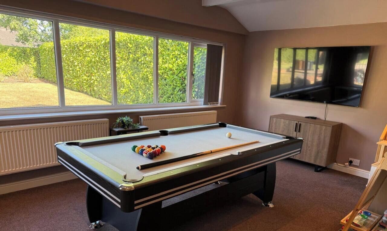 A pool table with balls, a television, and a window with a view of greenery.
