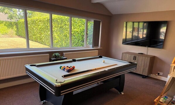 A pool table with balls, a television, and a window with a view of greenery. - Greenways House - Parking, Pool Table and Garden! (Wetley Rocks)