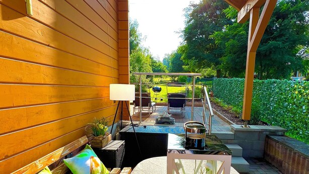 En træterrasse med en bænk, et bord og et glasindhegnet område med en plante.