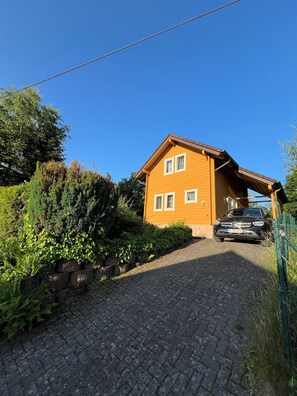 A house with a paved driveway, a car parked in front, and a clear blue sky. - AUSZEIT Country House, surrounded by nature, with a grill and fire pit (Borod)